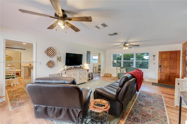 living room with ceiling fan, light hardwood / wood-style floors, and a textured ceiling