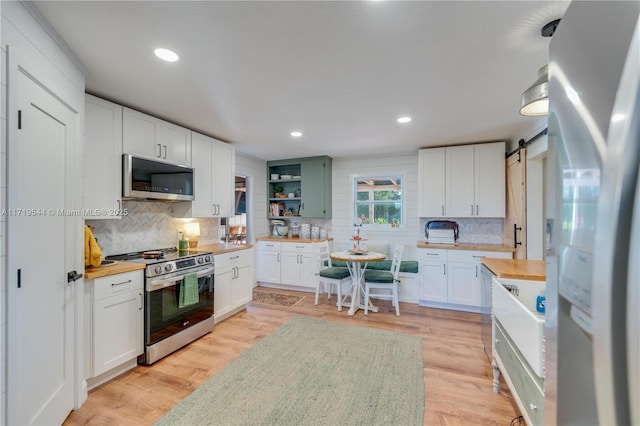 kitchen featuring stainless steel appliances, white cabinetry, a barn door, and wood counters