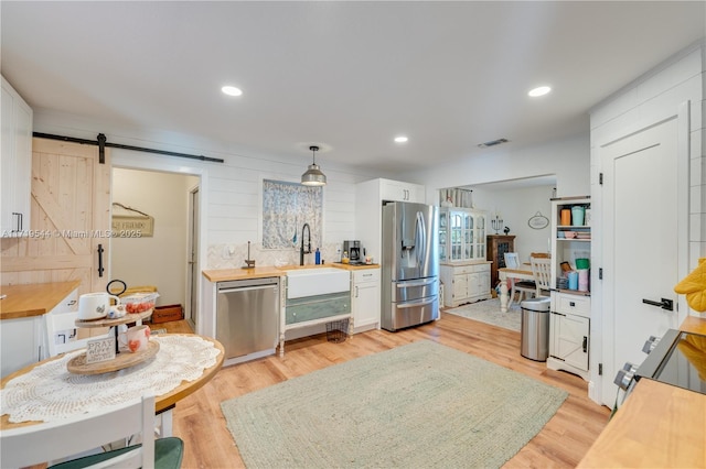 kitchen featuring appliances with stainless steel finishes, sink, white cabinets, a barn door, and light wood-type flooring