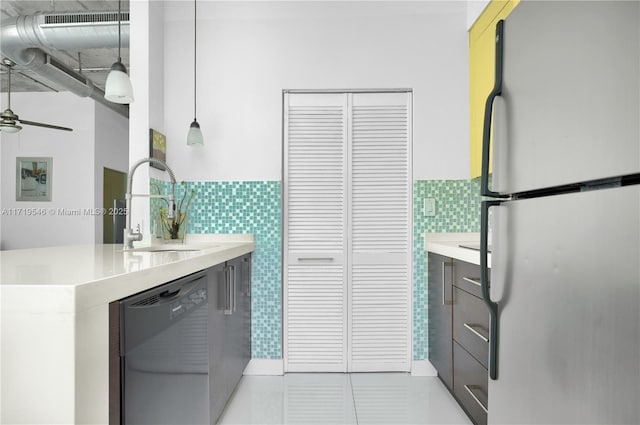 kitchen featuring light countertops, dishwashing machine, freestanding refrigerator, tile walls, and a sink