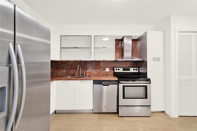 kitchen with appliances with stainless steel finishes, sink, wall chimney range hood, dark stone countertops, and white cabinetry