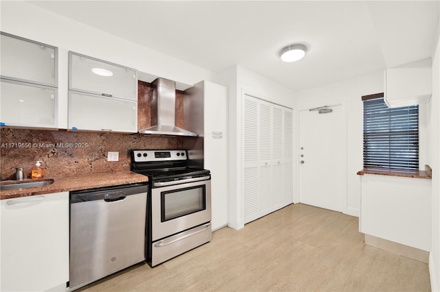 kitchen with tasteful backsplash, wall chimney exhaust hood, stainless steel appliances, sink, and white cabinetry