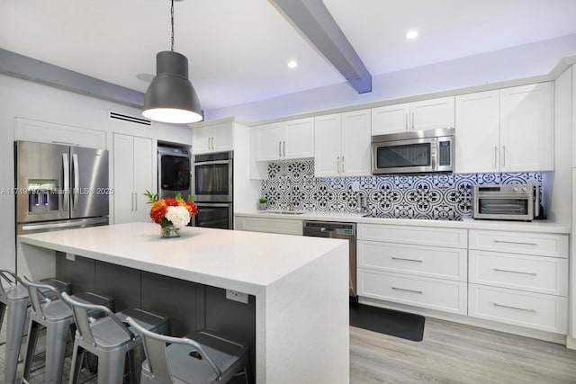 kitchen featuring white cabinetry, stainless steel appliances, decorative light fixtures, beam ceiling, and a center island