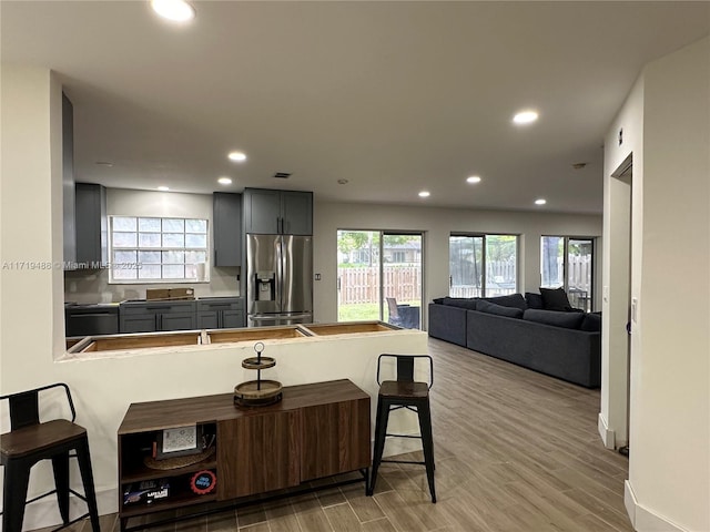 kitchen with kitchen peninsula, stainless steel fridge, a kitchen bar, gray cabinetry, and light hardwood / wood-style floors