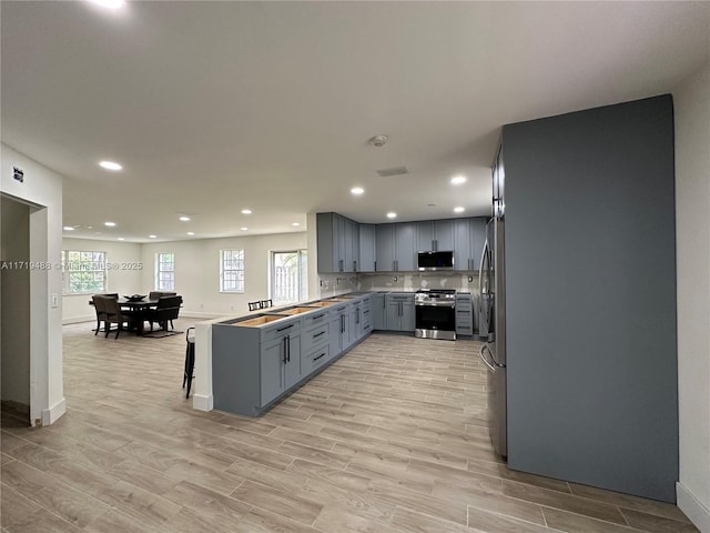 kitchen with kitchen peninsula, decorative backsplash, stainless steel appliances, and light wood-type flooring