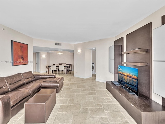 living room featuring baseboards, visible vents, washer / clothes dryer, a fireplace with raised hearth, and stone tile flooring