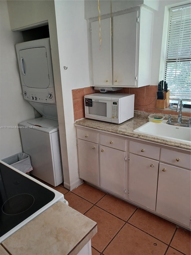 kitchen with stove, sink, light tile patterned floors, stacked washer and clothes dryer, and white cabinets