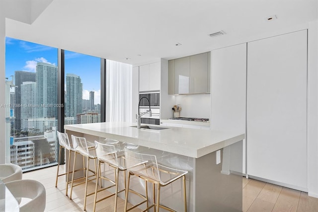 kitchen featuring a kitchen breakfast bar, sink, stainless steel gas cooktop, light wood-type flooring, and expansive windows