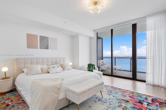 bedroom featuring a notable chandelier, floor to ceiling windows, access to outside, light wood-type flooring, and a water view