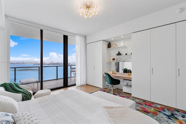 bedroom featuring light hardwood / wood-style floors, a wall of windows, access to outside, built in desk, and a water view