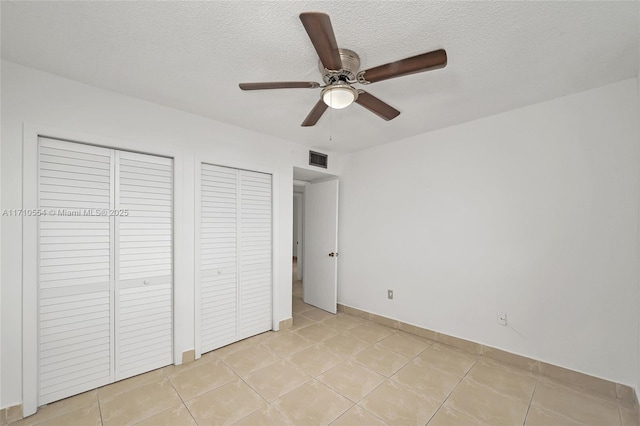 unfurnished bedroom featuring light tile patterned floors, a textured ceiling, two closets, and ceiling fan