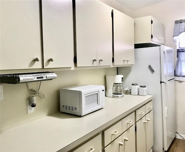 kitchen with white cabinets, hardwood / wood-style floors, and white appliances