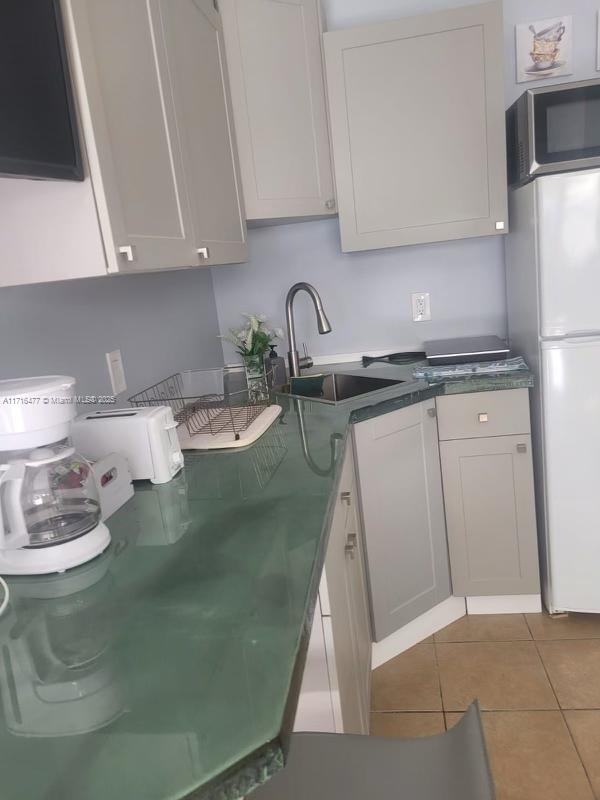 kitchen featuring light tile patterned flooring, white refrigerator, white cabinetry, and sink