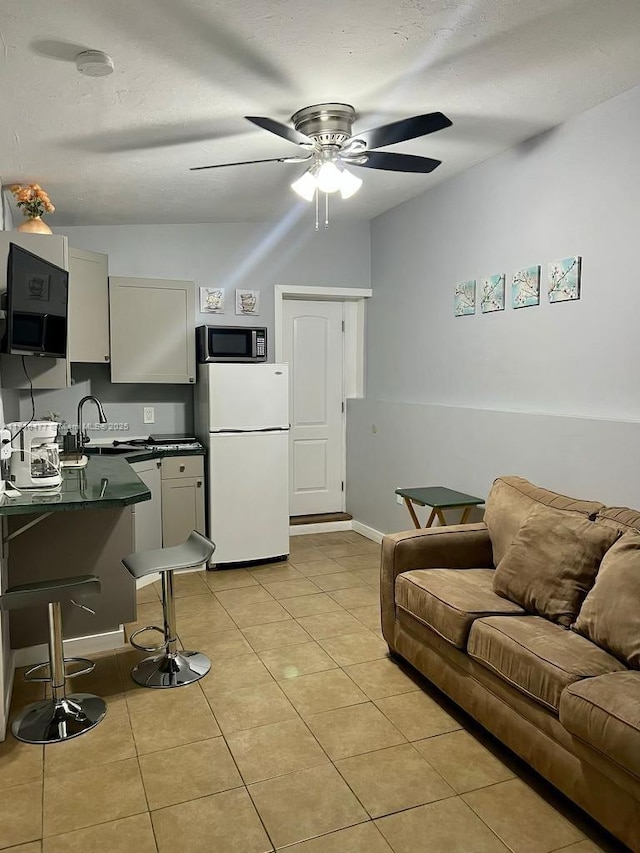 kitchen with light tile patterned floors, white refrigerator, white cabinetry, and ceiling fan