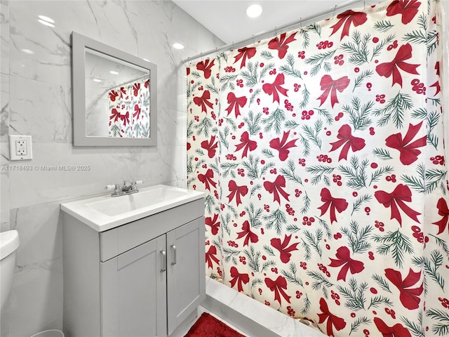 bathroom featuring vanity, toilet, walk in shower, and tile walls