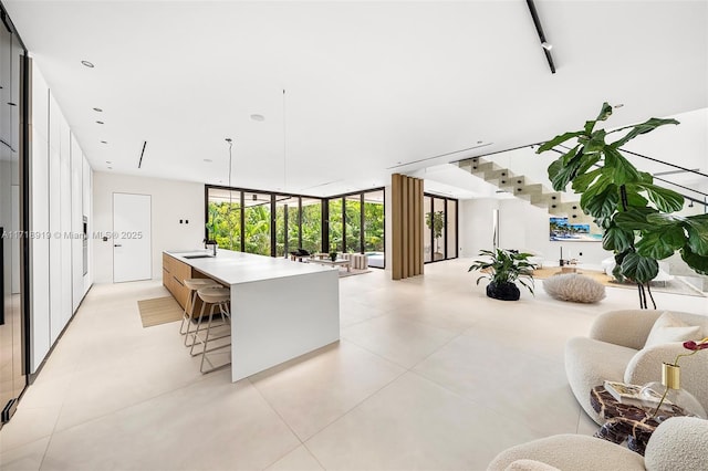 kitchen with hanging light fixtures, sink, a wall of windows, and an island with sink