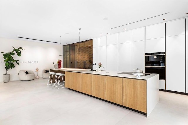 kitchen with white cabinets, a spacious island, hanging light fixtures, and black double oven