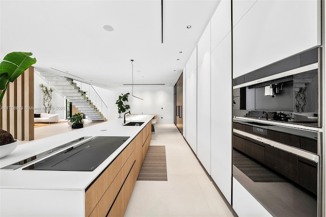 kitchen featuring white cabinetry, sink, hanging light fixtures, a large island with sink, and black electric stovetop