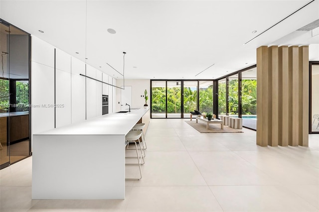 interior space featuring sink, hanging light fixtures, light tile patterned floors, a wall of windows, and white cabinets