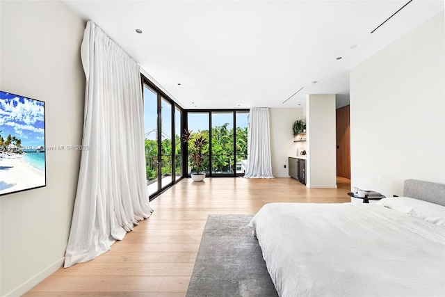 bedroom with access to outside, floor to ceiling windows, and light wood-type flooring