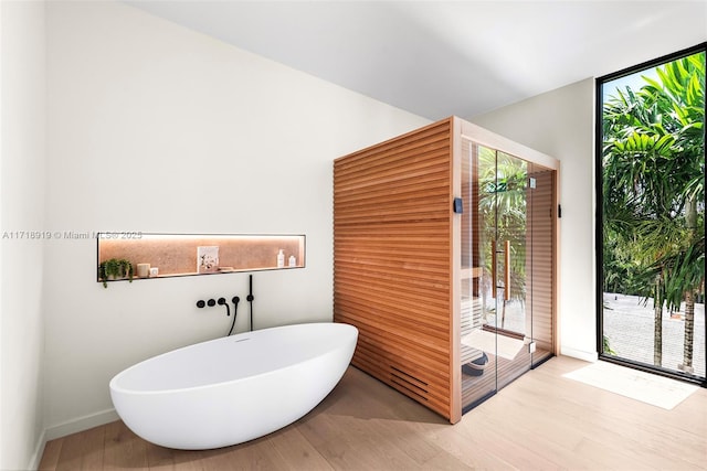 bathroom featuring wood-type flooring, floor to ceiling windows, and a bathing tub