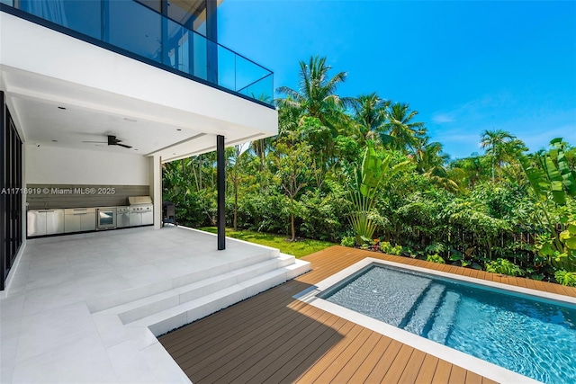 view of pool with area for grilling, a deck, ceiling fan, exterior kitchen, and a patio area