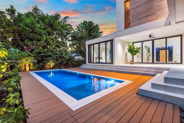 pool at dusk featuring ceiling fan and a deck