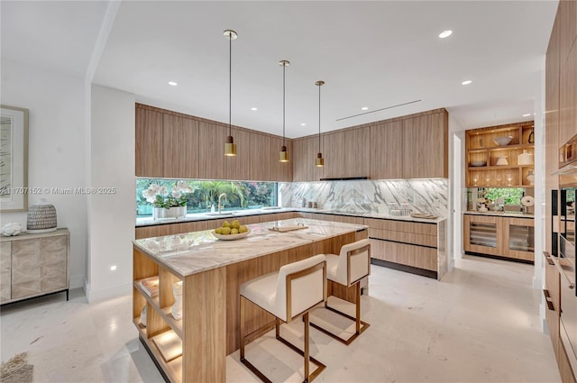 kitchen featuring pendant lighting, backsplash, a kitchen breakfast bar, light stone countertops, and a kitchen island