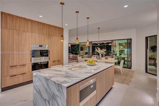 kitchen with a spacious island, hanging light fixtures, light stone countertops, light brown cabinetry, and stainless steel double oven