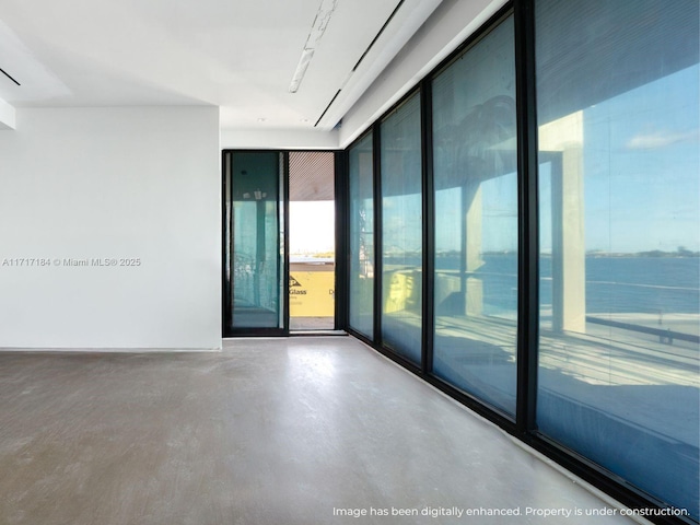 spare room with a wealth of natural light, a water view, and concrete flooring