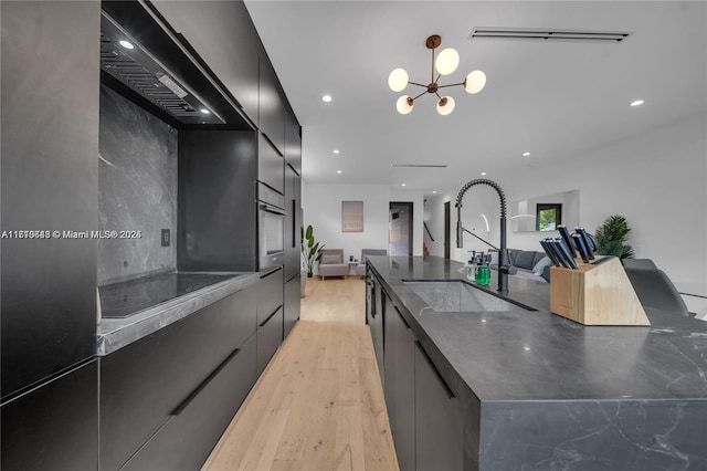 kitchen featuring black electric cooktop, sink, an inviting chandelier, light hardwood / wood-style floors, and oven