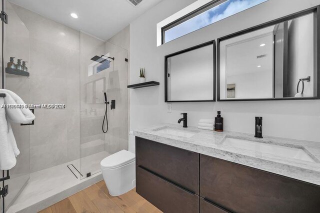 bathroom with vanity, toilet, a tile shower, and wood-type flooring