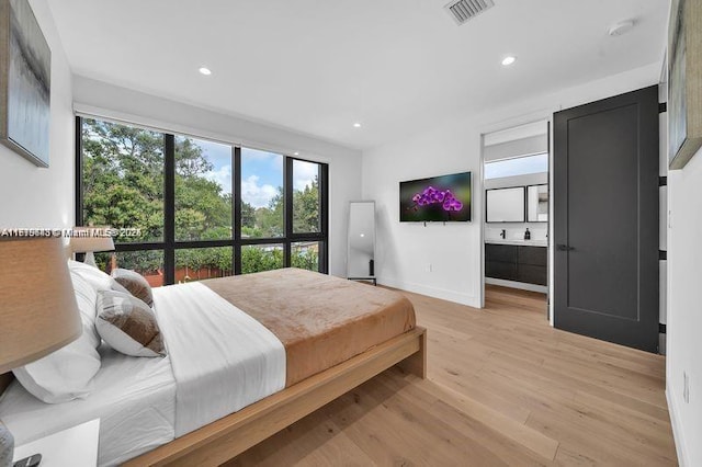 bedroom with ensuite bathroom and light hardwood / wood-style flooring