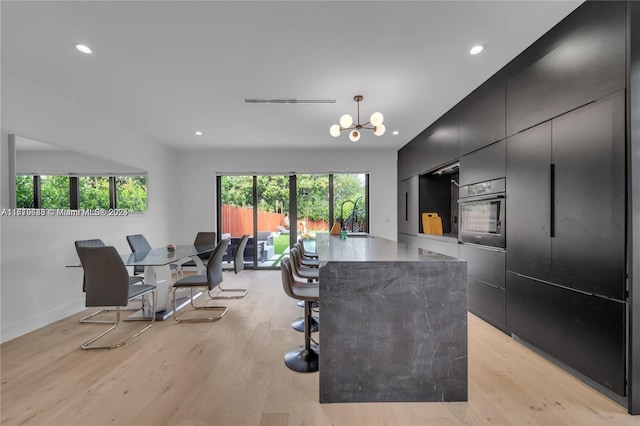 interior space with a center island, a kitchen breakfast bar, decorative light fixtures, light hardwood / wood-style flooring, and wall oven