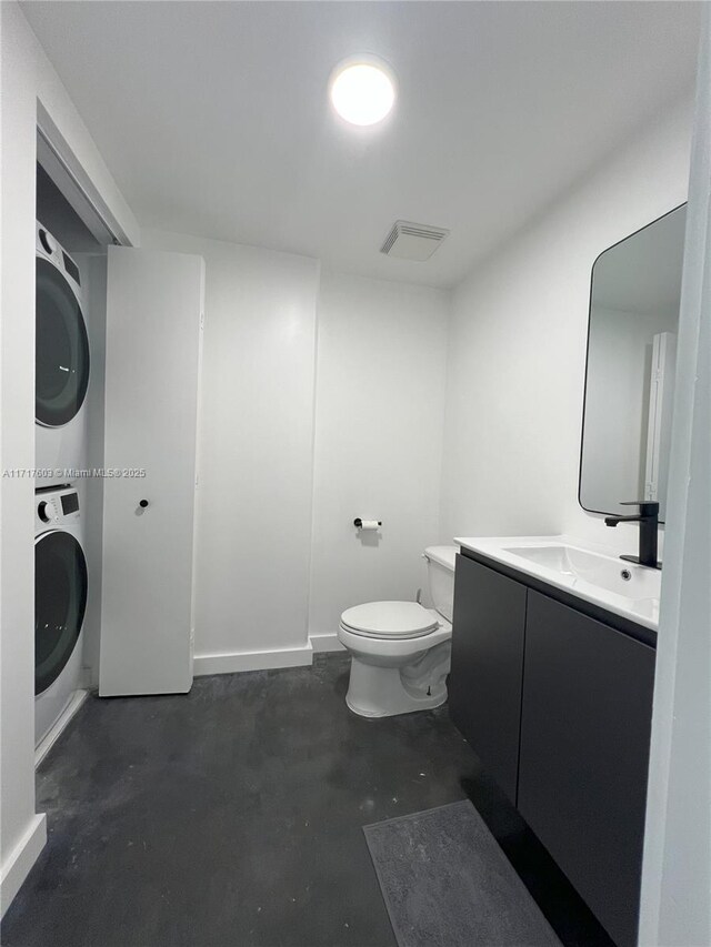 bathroom featuring toilet, stacked washing maching and dryer, concrete flooring, and vanity