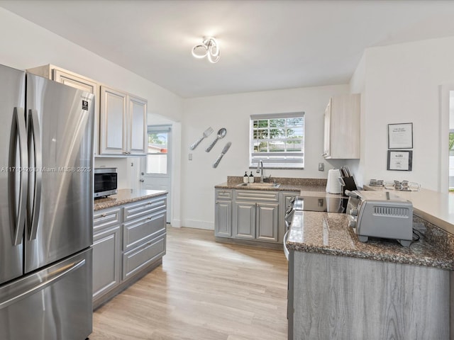 kitchen featuring sink, gray cabinetry, dark stone countertops, stainless steel appliances, and light hardwood / wood-style floors