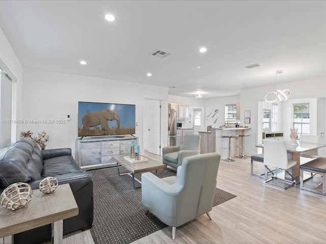 living room featuring a notable chandelier, light hardwood / wood-style flooring, and plenty of natural light