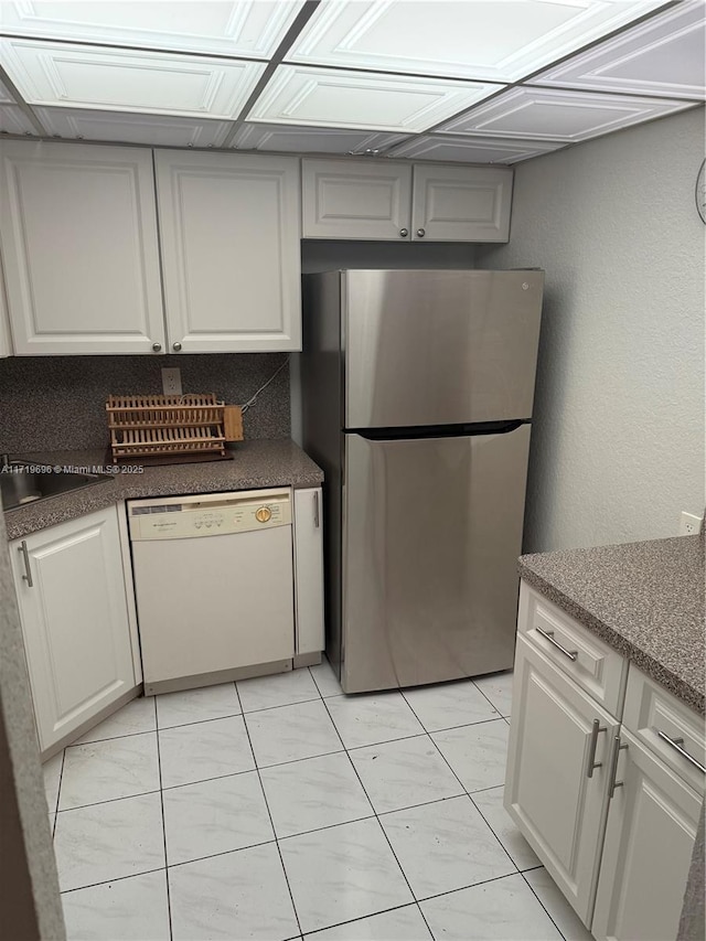 kitchen featuring white dishwasher, sink, white cabinets, stainless steel refrigerator, and light tile patterned flooring