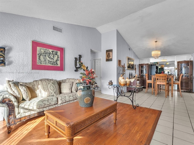 living room with a notable chandelier, light tile patterned floors, a textured ceiling, and vaulted ceiling