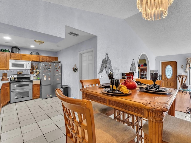 dining room with a chandelier, light tile patterned floors, a textured ceiling, and lofted ceiling