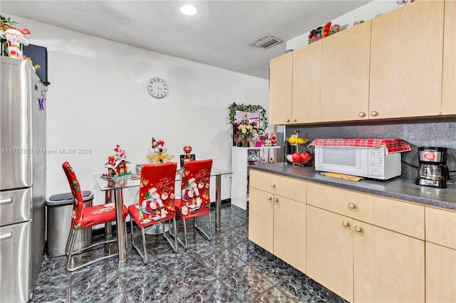 kitchen with stainless steel fridge, light brown cabinets, and a textured ceiling