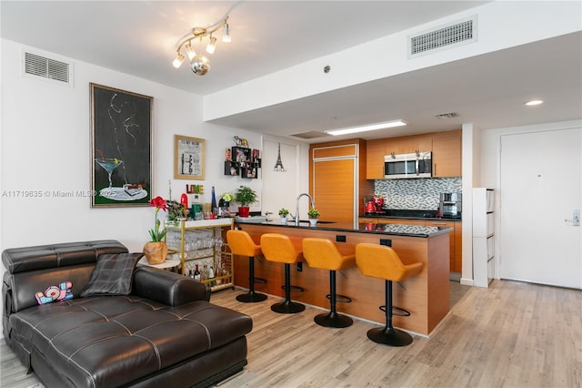 kitchen with decorative backsplash, kitchen peninsula, light hardwood / wood-style floors, and a breakfast bar area