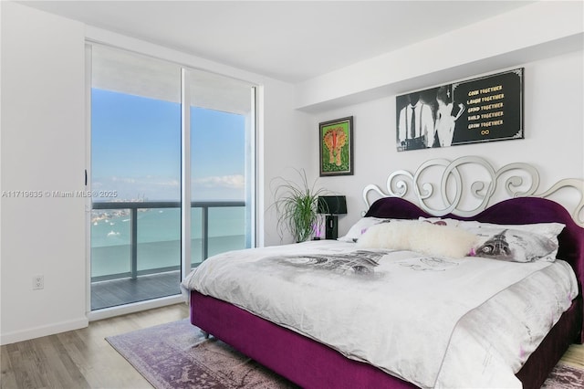 bedroom featuring access to exterior, light hardwood / wood-style flooring, expansive windows, and a water view