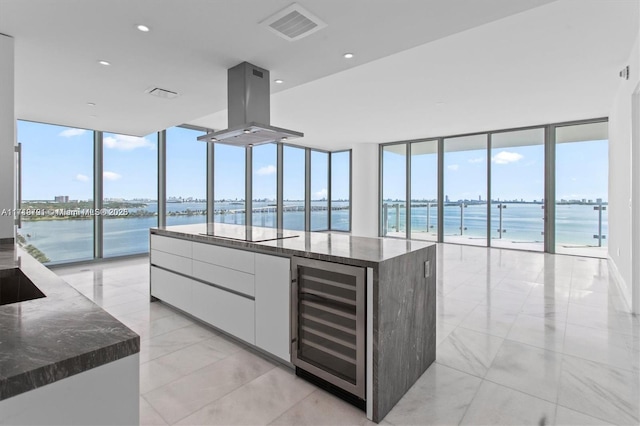 kitchen with wine cooler, white cabinets, dark stone counters, island range hood, and a water view