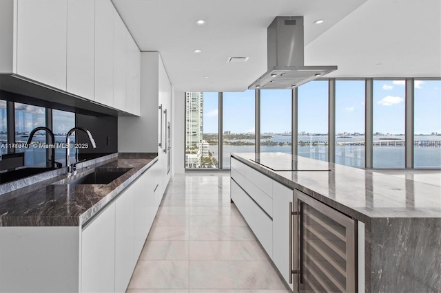 kitchen featuring floor to ceiling windows, island range hood, beverage cooler, and dark stone counters