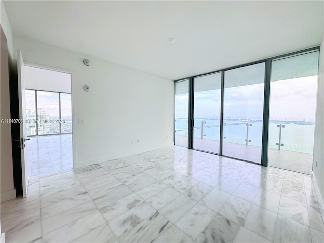 spare room featuring plenty of natural light, a water view, and a wall of windows