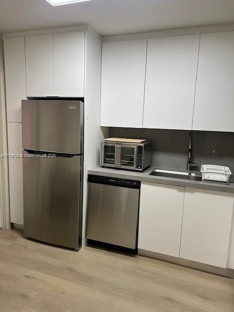 kitchen with white cabinets, appliances with stainless steel finishes, light hardwood / wood-style floors, and sink