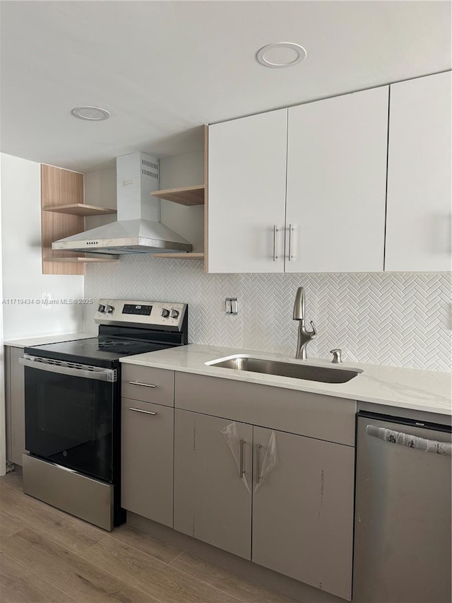 kitchen featuring open shelves, stainless steel appliances, decorative backsplash, a sink, and wall chimney range hood