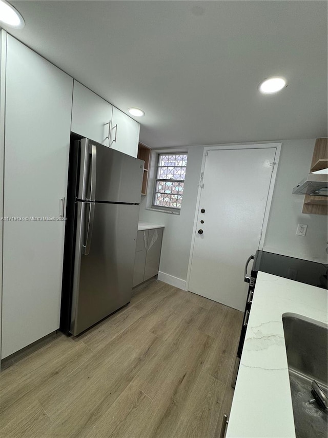 kitchen featuring light countertops, light wood-type flooring, freestanding refrigerator, and white cabinetry