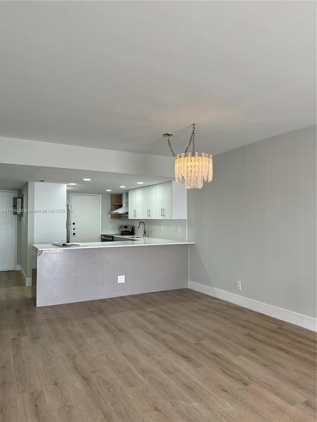 kitchen featuring light countertops, a sink, wood finished floors, a peninsula, and wall chimney exhaust hood